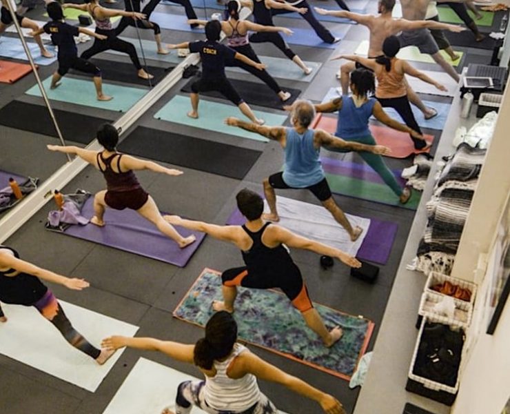 yoga room with multiple people practicing yoga, standing in warrior pose