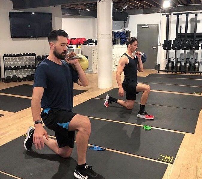 two men working out on black mats doing lunges