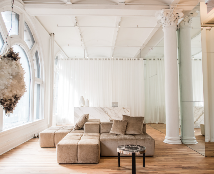 Interior of a yoga studio lobby. All white, wooden floors, brown couch and a large hanging crystal.