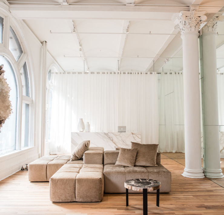 Interior of a yoga studio lobby. All white, wooden floors, brown couch and a large hanging crystal.