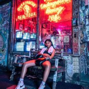 woman fighter with black hair sitting on a bench outside of a studio with a neon sigh that says Overthrow Boxing